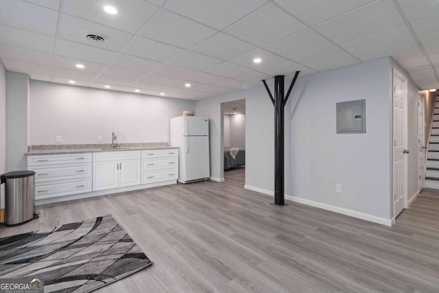 bar with light wood-style flooring, visible vents, baseboards, freestanding refrigerator, and electric panel