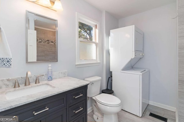 full bathroom featuring baseboards, visible vents, toilet, stacked washer / drying machine, and vanity