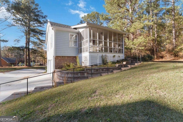 view of home's exterior featuring a yard, brick siding, and a sunroom