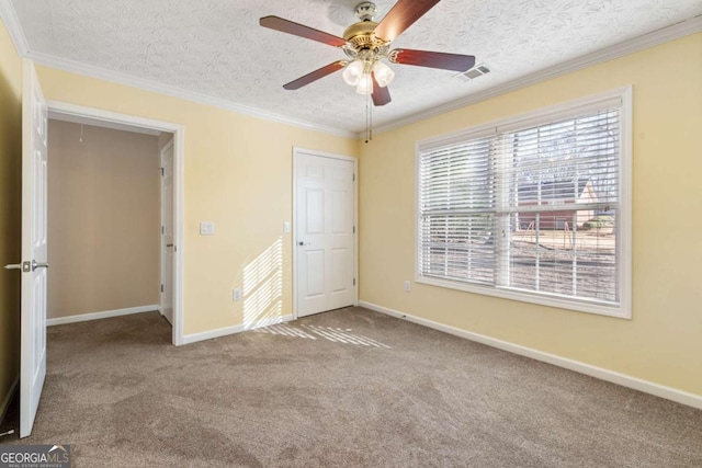 unfurnished bedroom with a textured ceiling, carpet floors, visible vents, baseboards, and crown molding