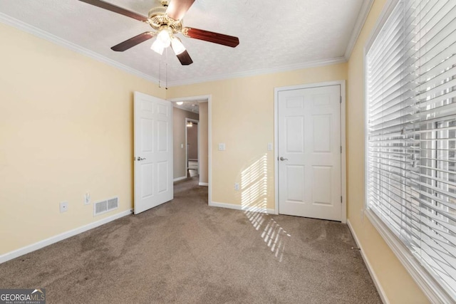 unfurnished bedroom with baseboards, visible vents, a textured ceiling, crown molding, and carpet floors