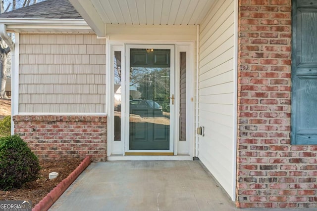 property entrance with a shingled roof and brick siding