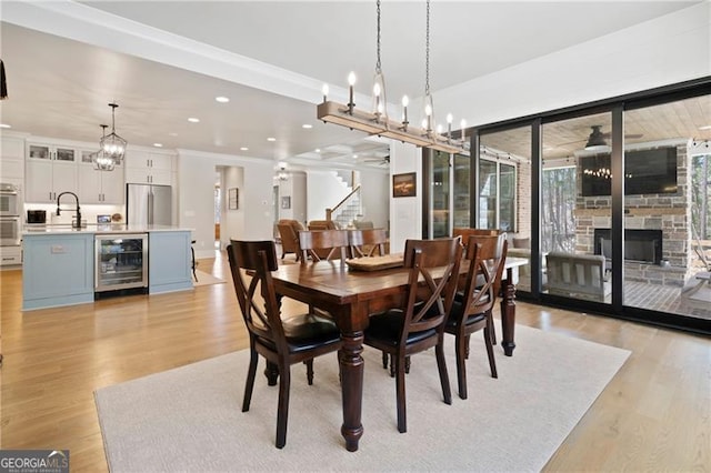 dining room with light wood-style flooring, recessed lighting, beverage cooler, and a stone fireplace