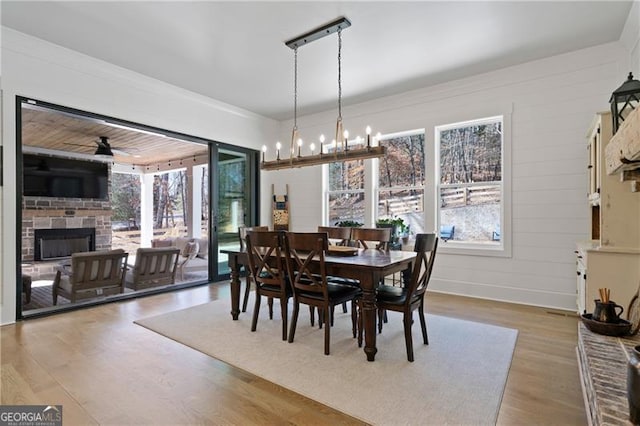 dining space featuring a fireplace with raised hearth, crown molding, wood finished floors, and a healthy amount of sunlight