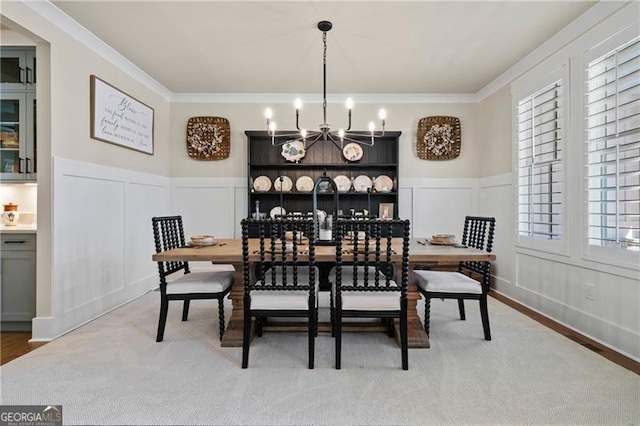 dining area with an inviting chandelier, a decorative wall, crown molding, and wainscoting