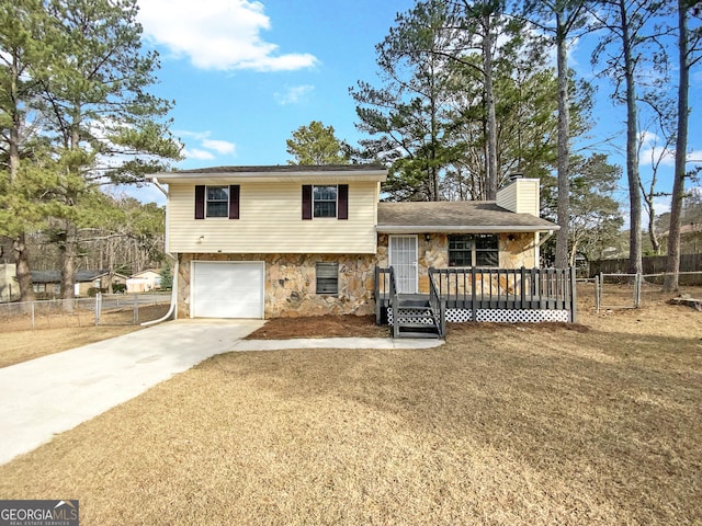 tri-level home with driveway, stone siding, a chimney, and fence