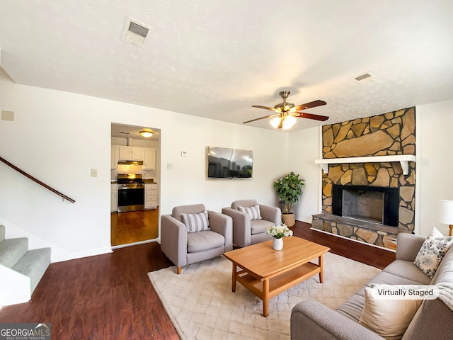 living room with a textured ceiling, visible vents, wood finished floors, and a stone fireplace