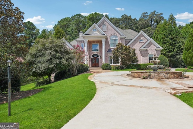 view of front of property with driveway, brick siding, a chimney, and a front yard