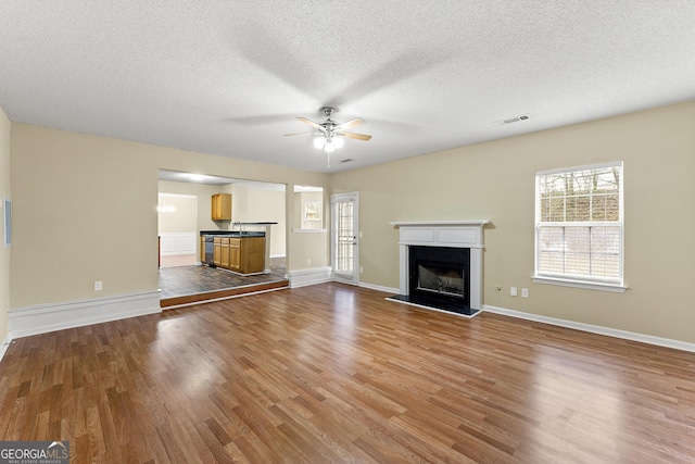 unfurnished living room featuring ceiling fan, a fireplace, baseboards, and wood finished floors