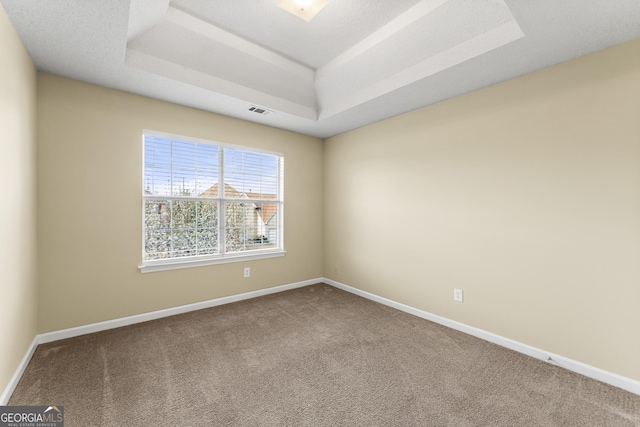 carpeted empty room featuring a tray ceiling, visible vents, and baseboards