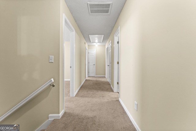 corridor with attic access, visible vents, baseboards, and light colored carpet