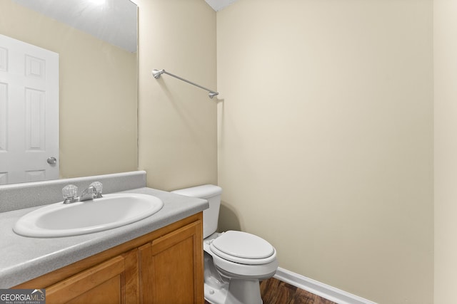 half bath featuring wood finished floors, vanity, toilet, and baseboards