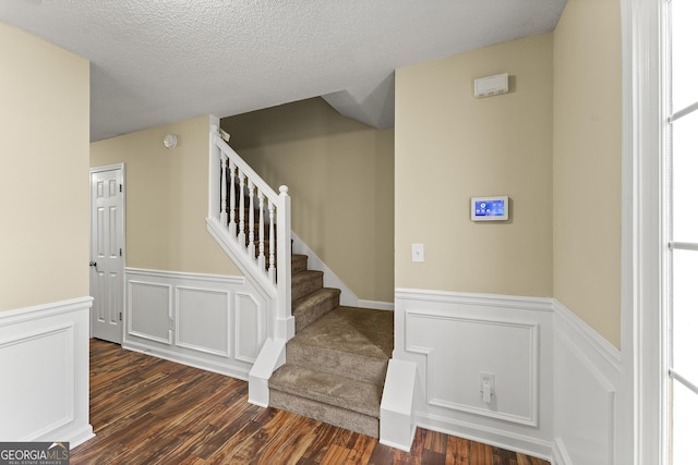 stairway with a textured ceiling, a wainscoted wall, and wood finished floors