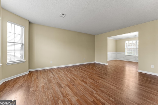 empty room with an inviting chandelier, a textured ceiling, visible vents, and wood finished floors