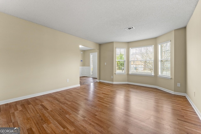 spare room featuring visible vents, a textured ceiling, baseboards, and wood finished floors