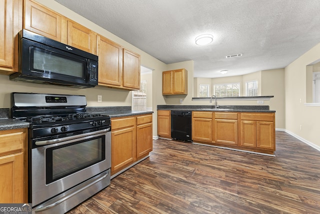 kitchen with black appliances, dark countertops, a sink, and visible vents