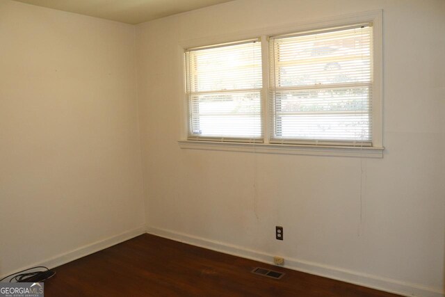 spare room featuring dark wood-style floors, visible vents, and baseboards