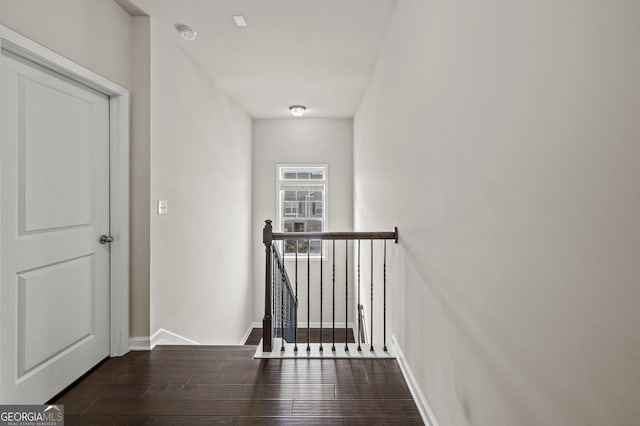 hallway with dark wood-style floors, baseboards, and an upstairs landing