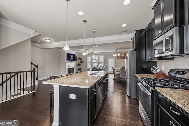 kitchen featuring pendant lighting, stainless steel appliances, a kitchen island with sink, a sink, and dark cabinetry