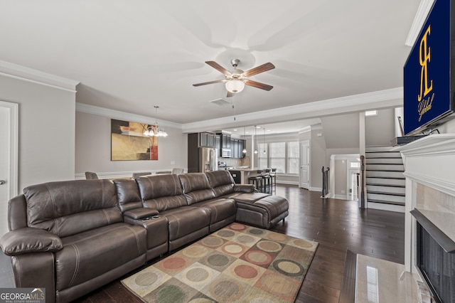 living area with crown molding, dark wood finished floors, a fireplace, visible vents, and ceiling fan with notable chandelier