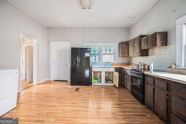 kitchen featuring light wood-style flooring, dark brown cabinetry, light countertops, black appliances, and washer / dryer