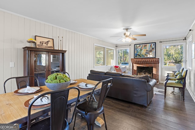 dining space with ceiling fan, a fireplace, ornamental molding, and dark wood finished floors