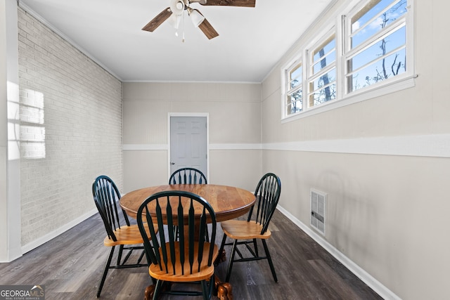 dining room with ceiling fan, brick wall, visible vents, baseboards, and dark wood-style floors