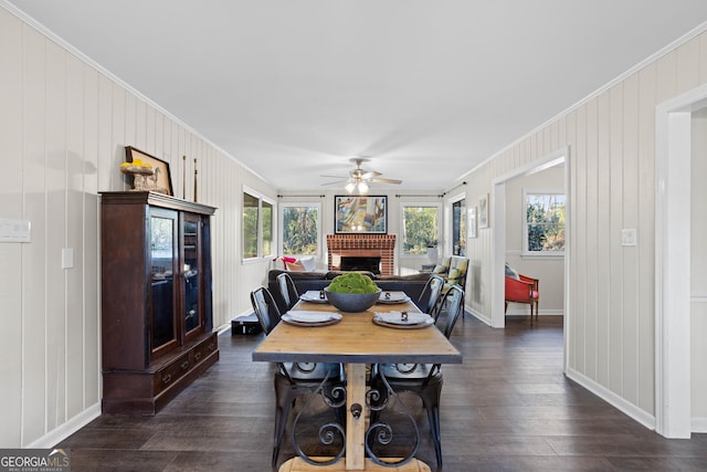 dining space featuring baseboards, a ceiling fan, dark wood-style flooring, crown molding, and a fireplace