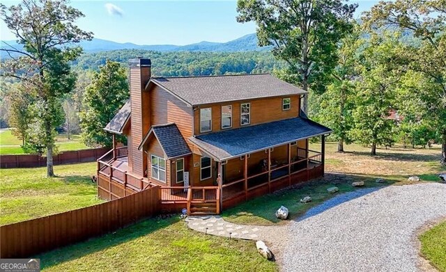 rear view of property featuring a deck with mountain view, driveway, a yard, and a chimney