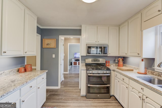 kitchen featuring stainless steel appliances, a sink, baseboards, ornamental molding, and light wood finished floors