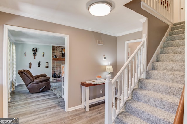 stairway with a fireplace, crown molding, baseboards, and wood finished floors