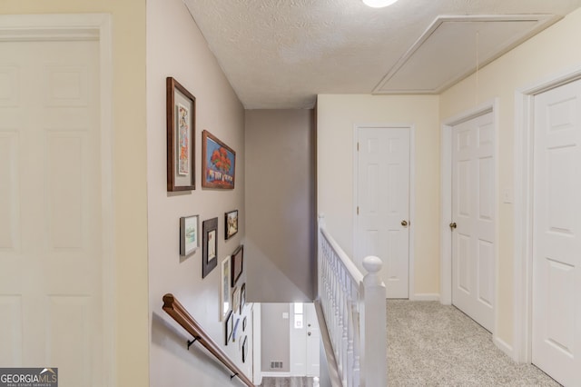 hallway featuring attic access, light carpet, a textured ceiling, an upstairs landing, and baseboards