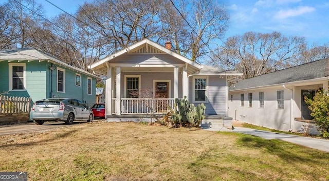 bungalow with covered porch, a front lawn, and a chimney