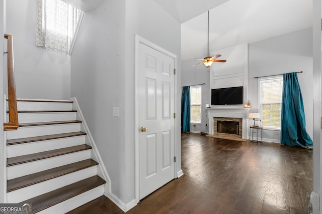 staircase featuring plenty of natural light, a ceiling fan, a fireplace with raised hearth, and wood finished floors