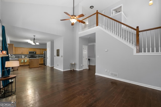 unfurnished living room with baseboards, visible vents, dark wood-style floors, a high ceiling, and ceiling fan with notable chandelier