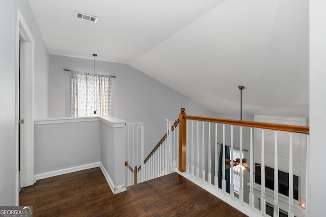 hallway featuring dark wood-type flooring, visible vents, vaulted ceiling, and an upstairs landing