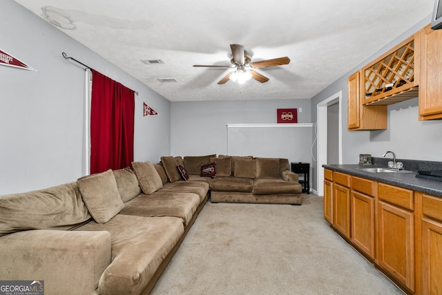 living room featuring light colored carpet, ceiling fan, visible vents, and a textured ceiling