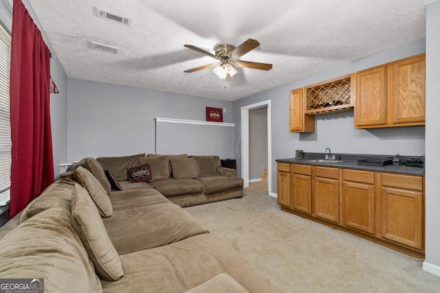 living area with light colored carpet, visible vents, ceiling fan, and a textured ceiling