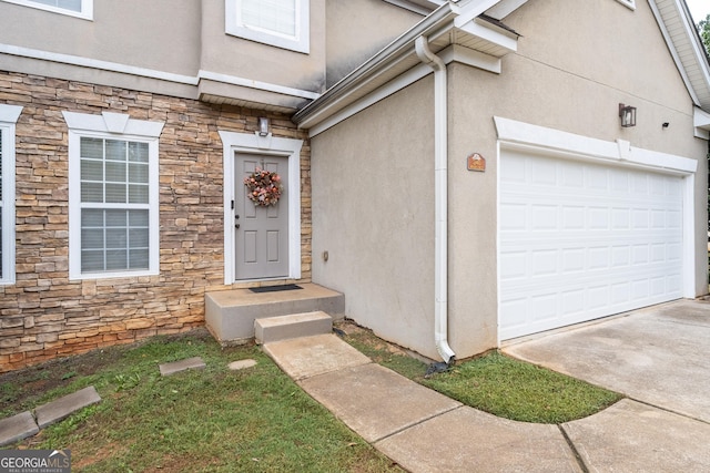 doorway to property featuring stone siding, an attached garage, and stucco siding