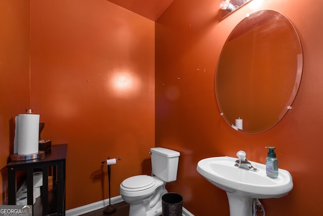 half bath with baseboards, a sink, and toilet