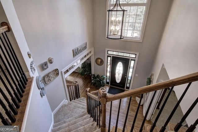 foyer featuring stairway, a towering ceiling, wood finished floors, a chandelier, and baseboards