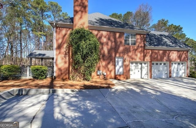 view of side of property with a garage, driveway, a chimney, and brick siding