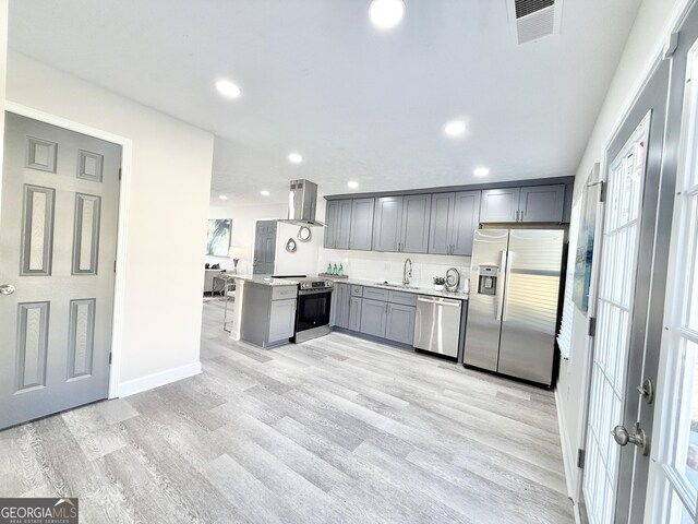 kitchen featuring stainless steel appliances, a sink, island range hood, a peninsula, and a kitchen bar