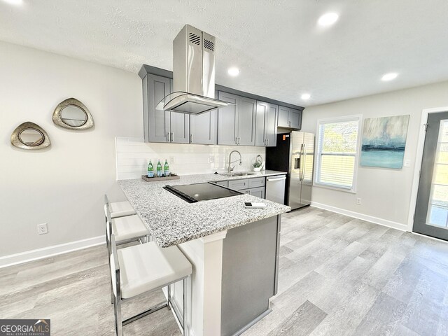 kitchen featuring island range hood, stainless steel appliances, a sink, gray cabinets, and light stone countertops