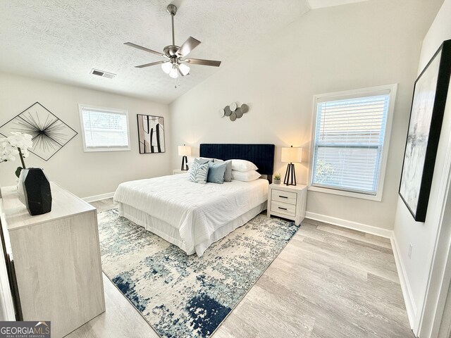 bedroom with baseboards, visible vents, lofted ceiling, light wood-style flooring, and a textured ceiling