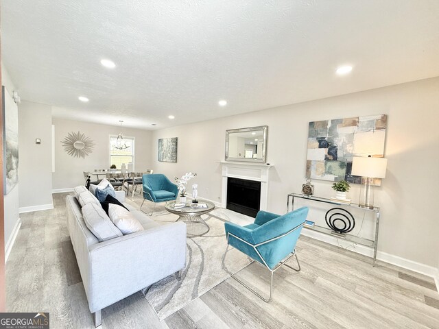 living room with baseboards, a fireplace with flush hearth, stairs, a textured ceiling, and light wood-style floors