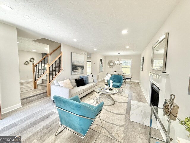 living area featuring light wood-style floors, a fireplace with flush hearth, baseboards, and a textured ceiling