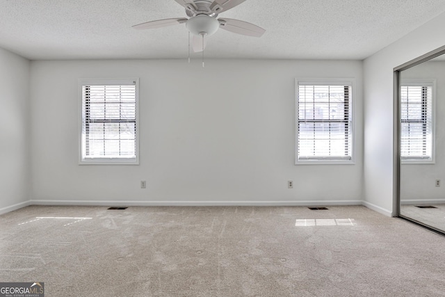 spare room with visible vents, light carpet, ceiling fan, a textured ceiling, and baseboards