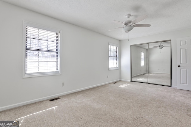 unfurnished bedroom featuring a closet, light colored carpet, visible vents, a textured ceiling, and baseboards