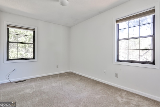 spare room featuring light carpet, plenty of natural light, and visible vents